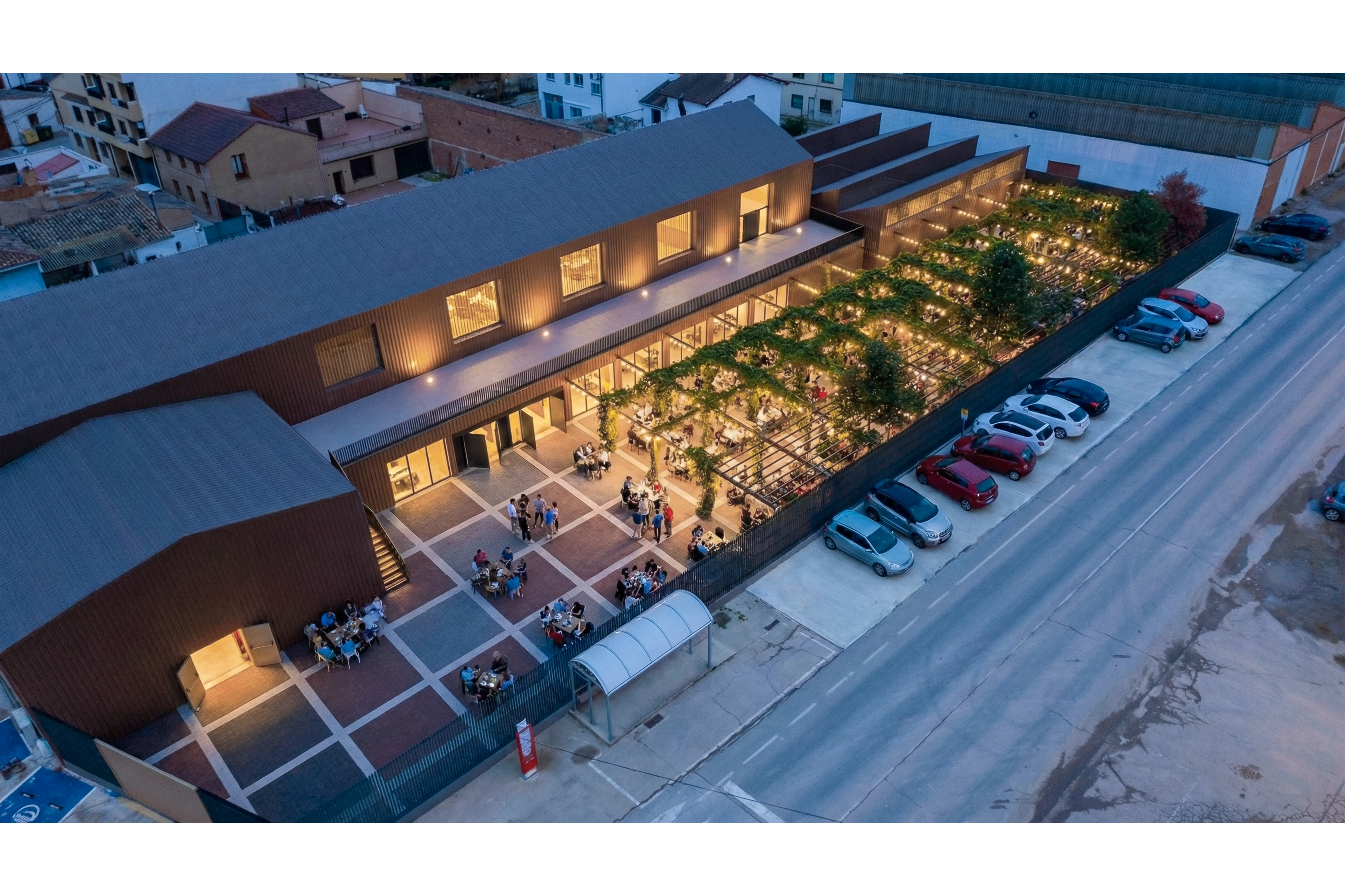 Render aéreo al anochecer del exterior del pabellón, mostrando la plaza iluminada, una gran pérgola y la plaza.
